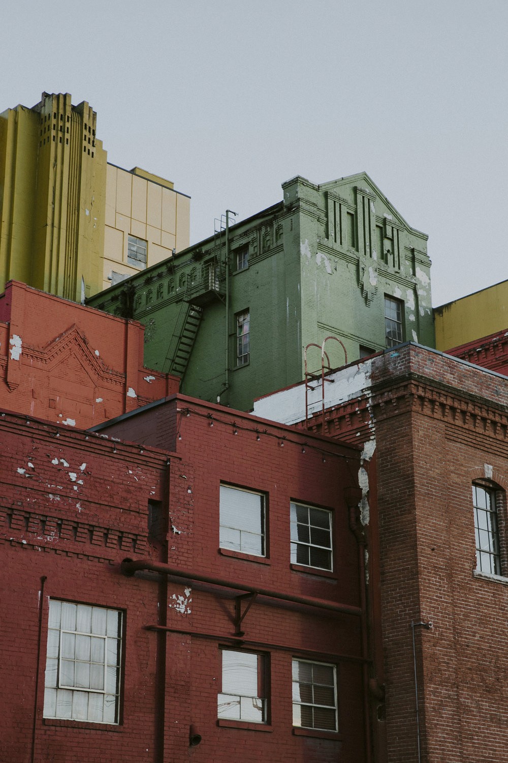 Colorful, peeling facades of Old Rainier Brewery in Seattle, showing red, green, and yellow weathered brick architecture under a clear sky.