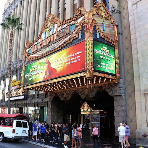 人们站在剧院华丽的入口前，门廊上广告着电影《雷神：诸神黄昏》。