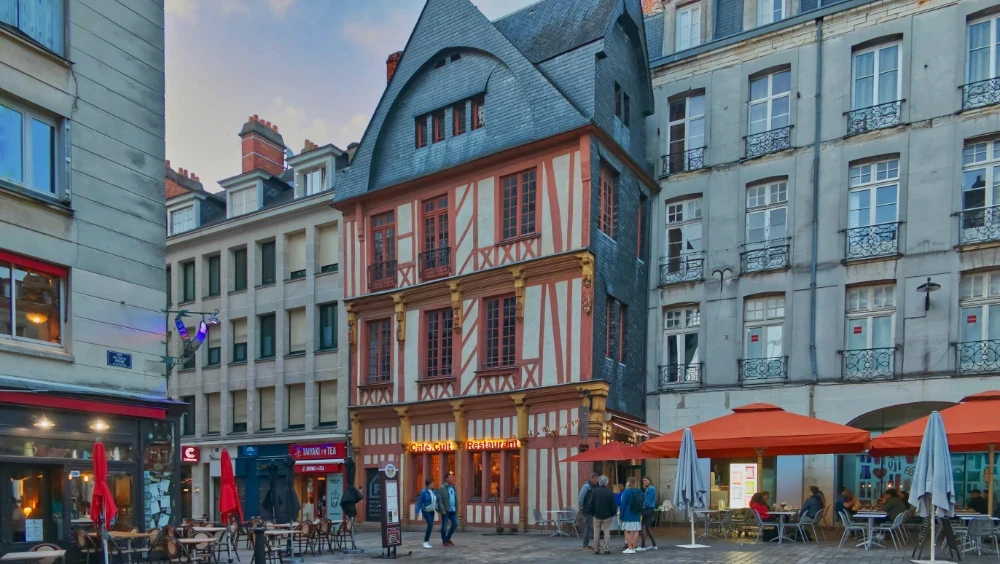 Lively French town square at dusk with a half-timbered medieval building and cafe terraces