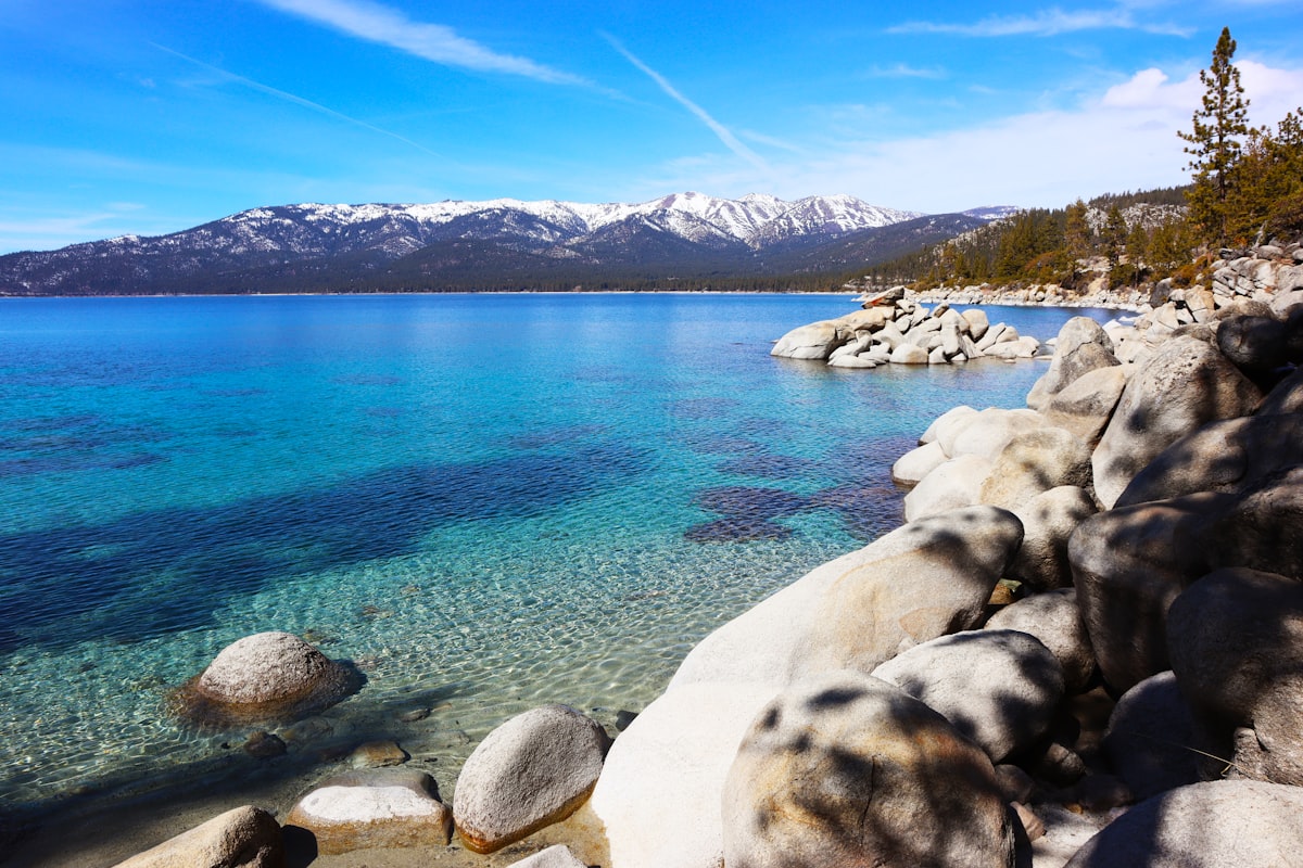 Clear blue water and boulders along Lake Tahoe's shoreline with mountains behind