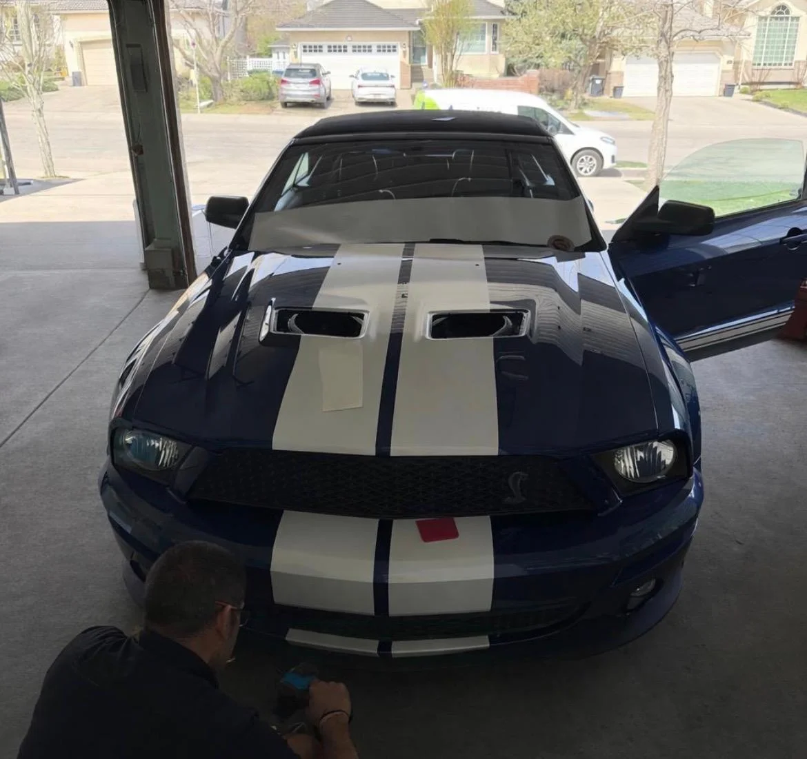 Blue Mustang with white stripes, man working on it
