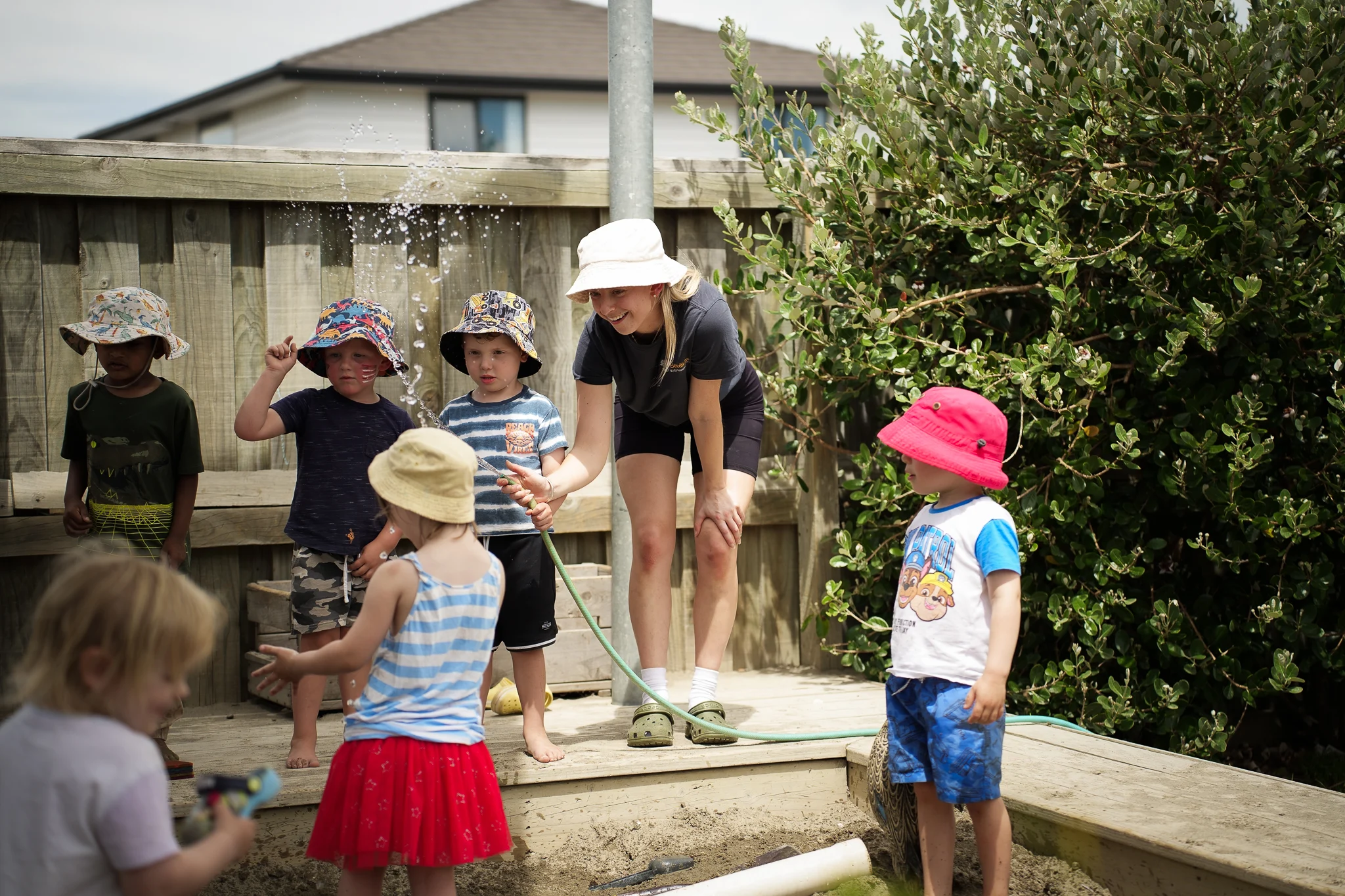Young children engage in supervised water play with a teacher in an outdoor early childhood environment.