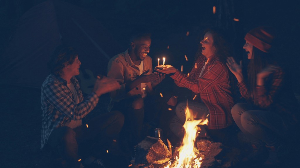 Friends celebrating birthday around campfire at night