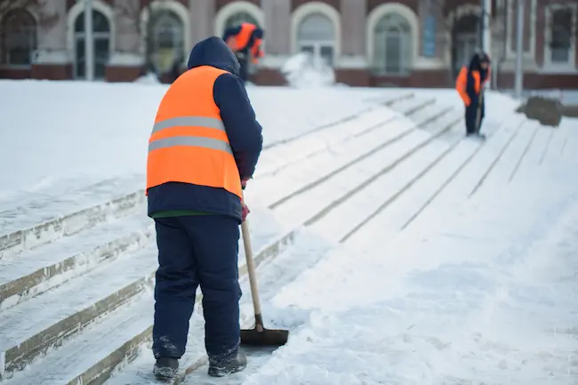 workers shovel snow from stairs in winter cleaning