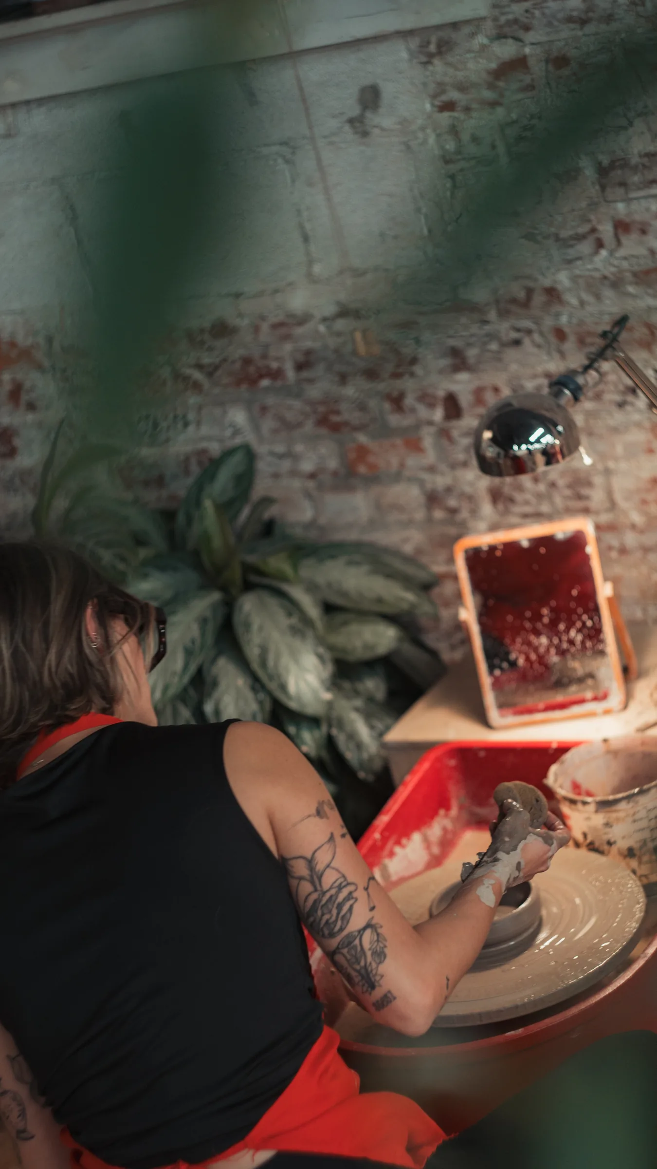 Member throwing on a pottery wheel that faces an exposed brick wall at Kinship Studio