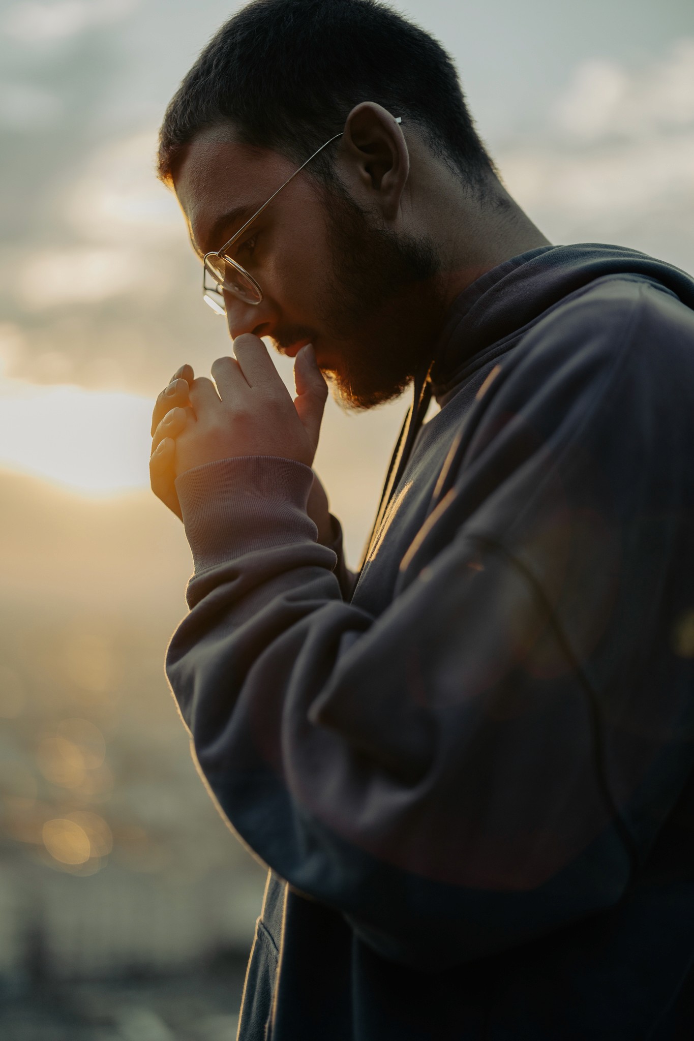 Férfi napsütésben, kapucnis pulóverben, oldalról, elmélyült pillanatban.