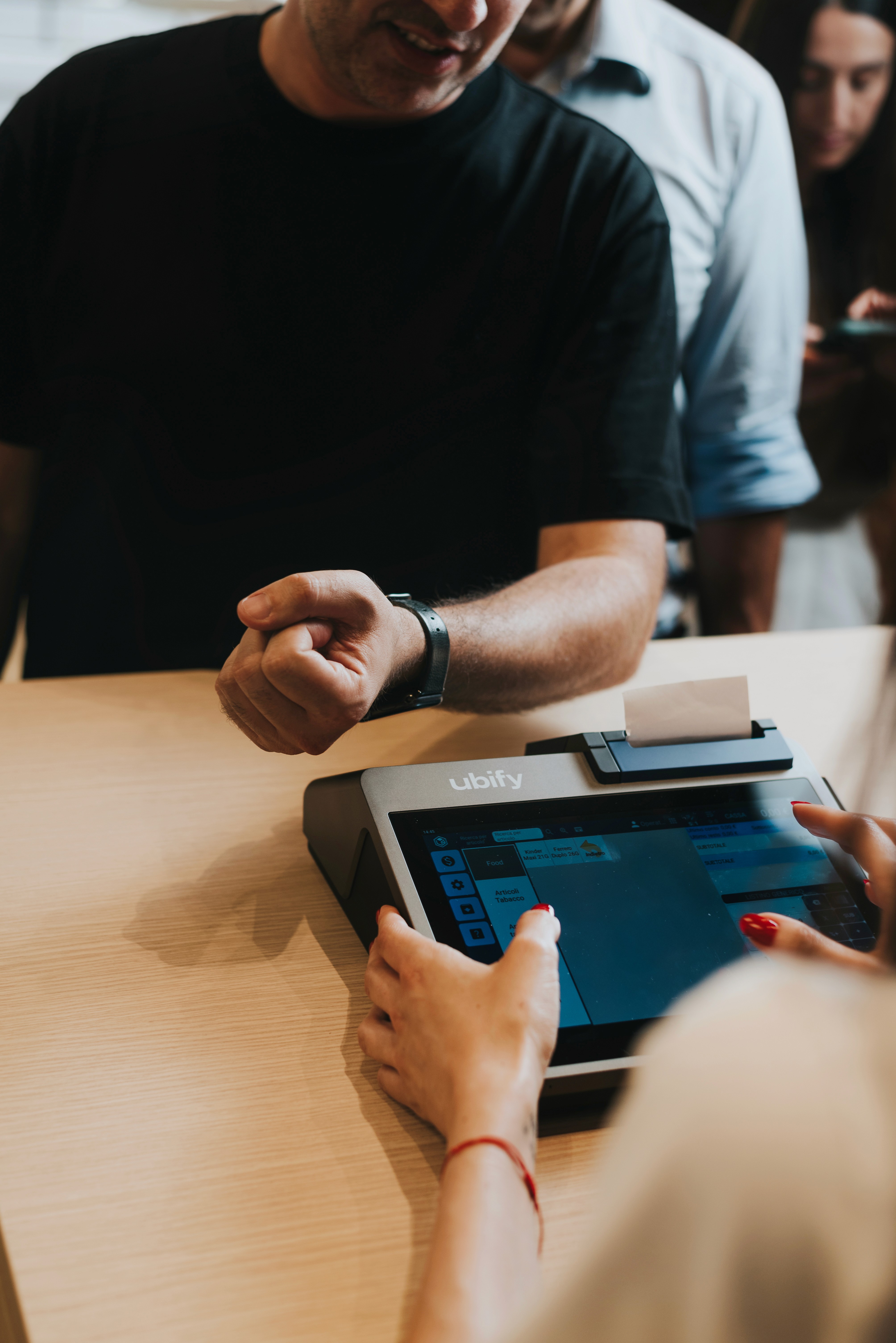 Cliente effettua un pagamento con smartwatch alla Cassa Ubify, mentre l’operatore completa l’operazione sul touchscreen.