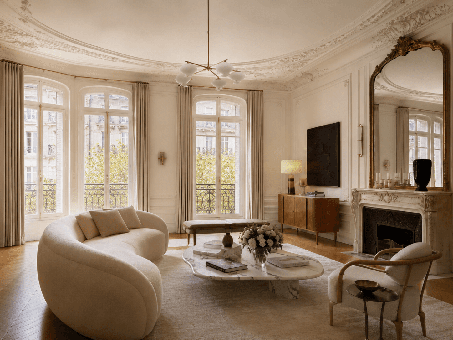 Bright Parisian Haussmann living room viewed from a different angle, featuring arched windows, herringbone wood floors, marble coffee table, and neutral luxury decor.