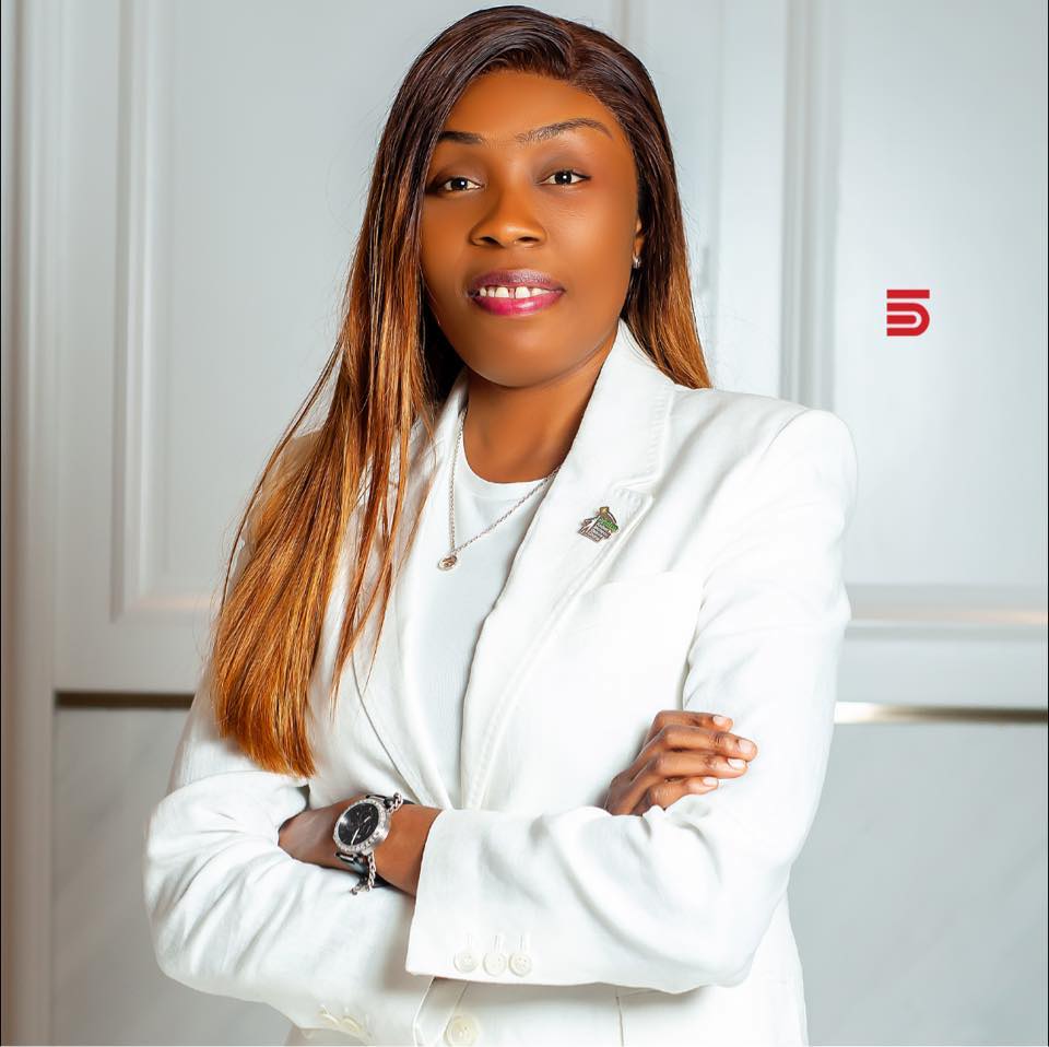 A confident person with short, styled hair and a leather jacket poses against a dark backdrop.