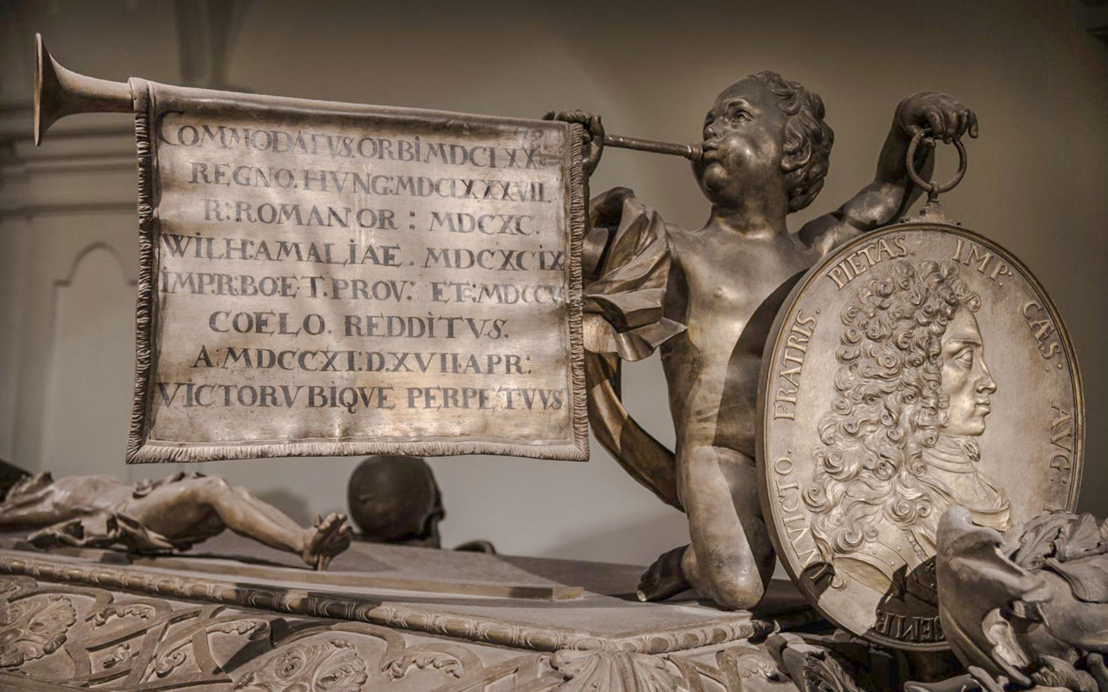 维也纳小修道院教堂内的雕塑细节，展示了一个手持小号和带有铭文横幅的天使。