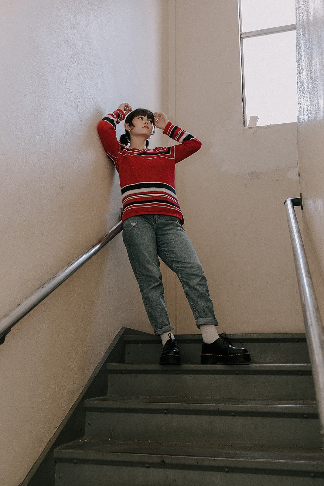 Model in red and striped sweater poses thoughtfully on a staircase at Revelator Studio in Shreveport for a 90s-inspired shoot.