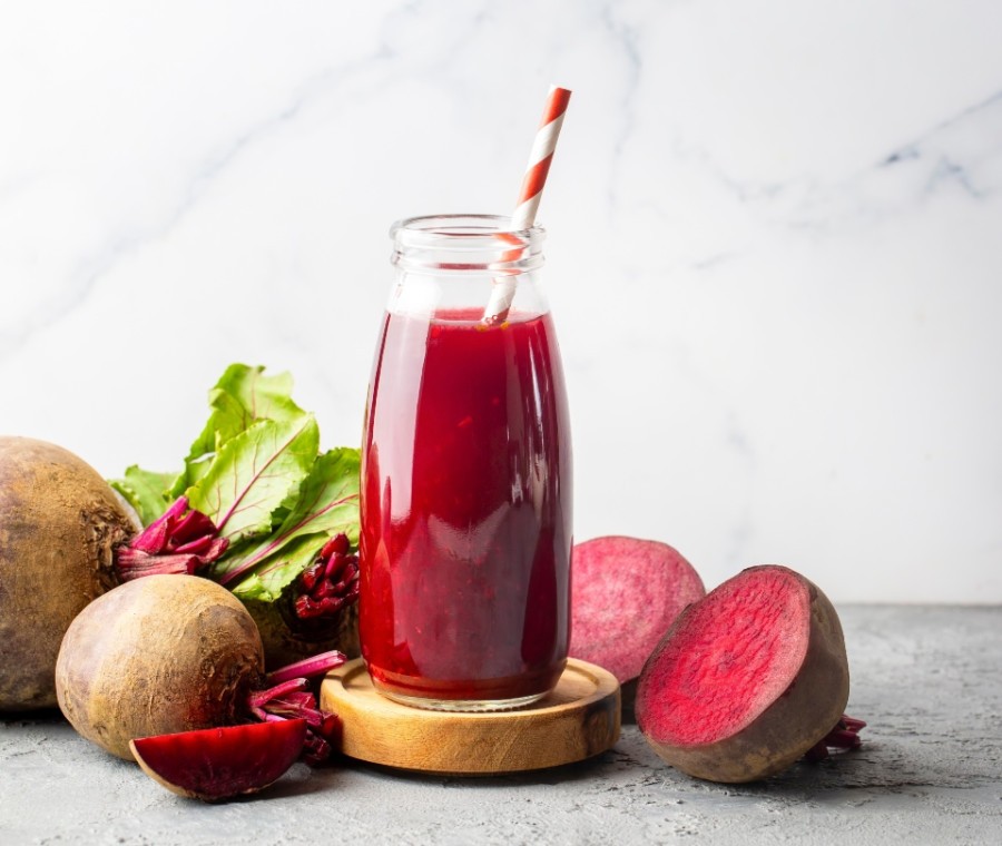 A wooden desk by a window, with sunlight illuminating a laptop, notebook, and a decorative vase.