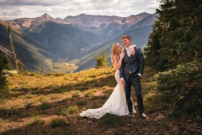 Clemmie leans against Tucker's shoulder as they stand above the mountain valley.