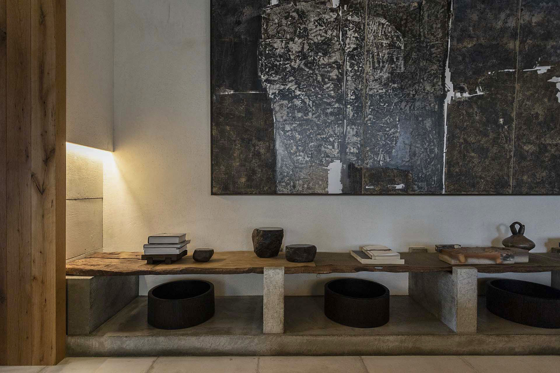 微光照明下的展示平台陳列書籍與陶器，搭配深色抽象畫與原木天花板展現侘寂氛圍