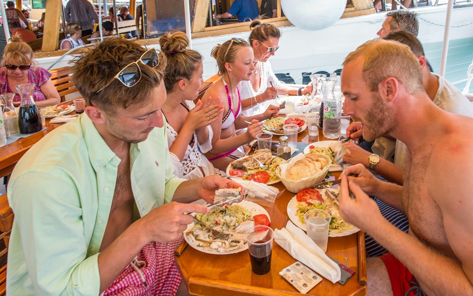 Passengers dining on a boat with plates of fish, salad, and bread.