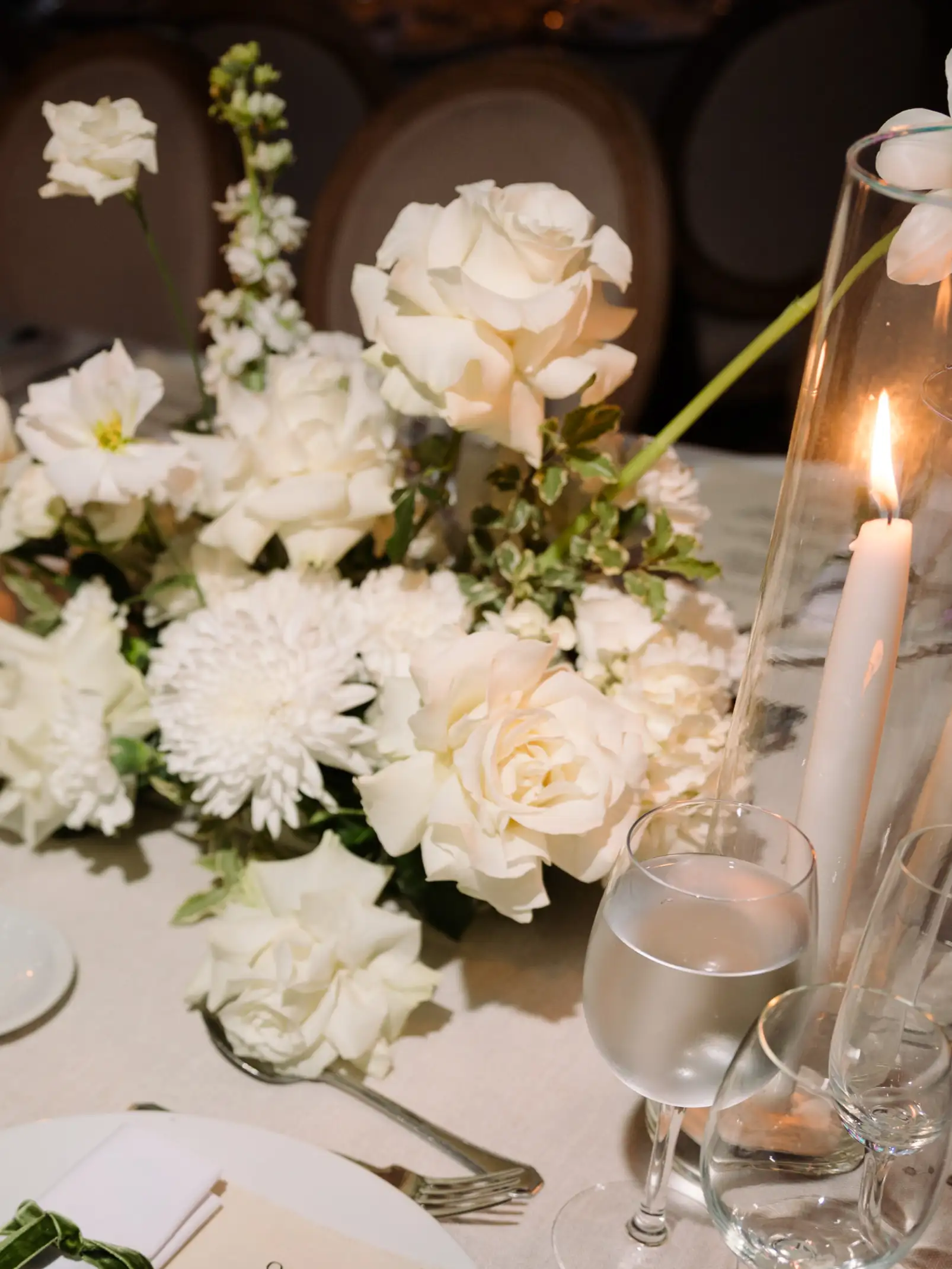 Centro de mesa con flores blancas, velas encendidas y copas de cristal sobre mantel de lino claro.