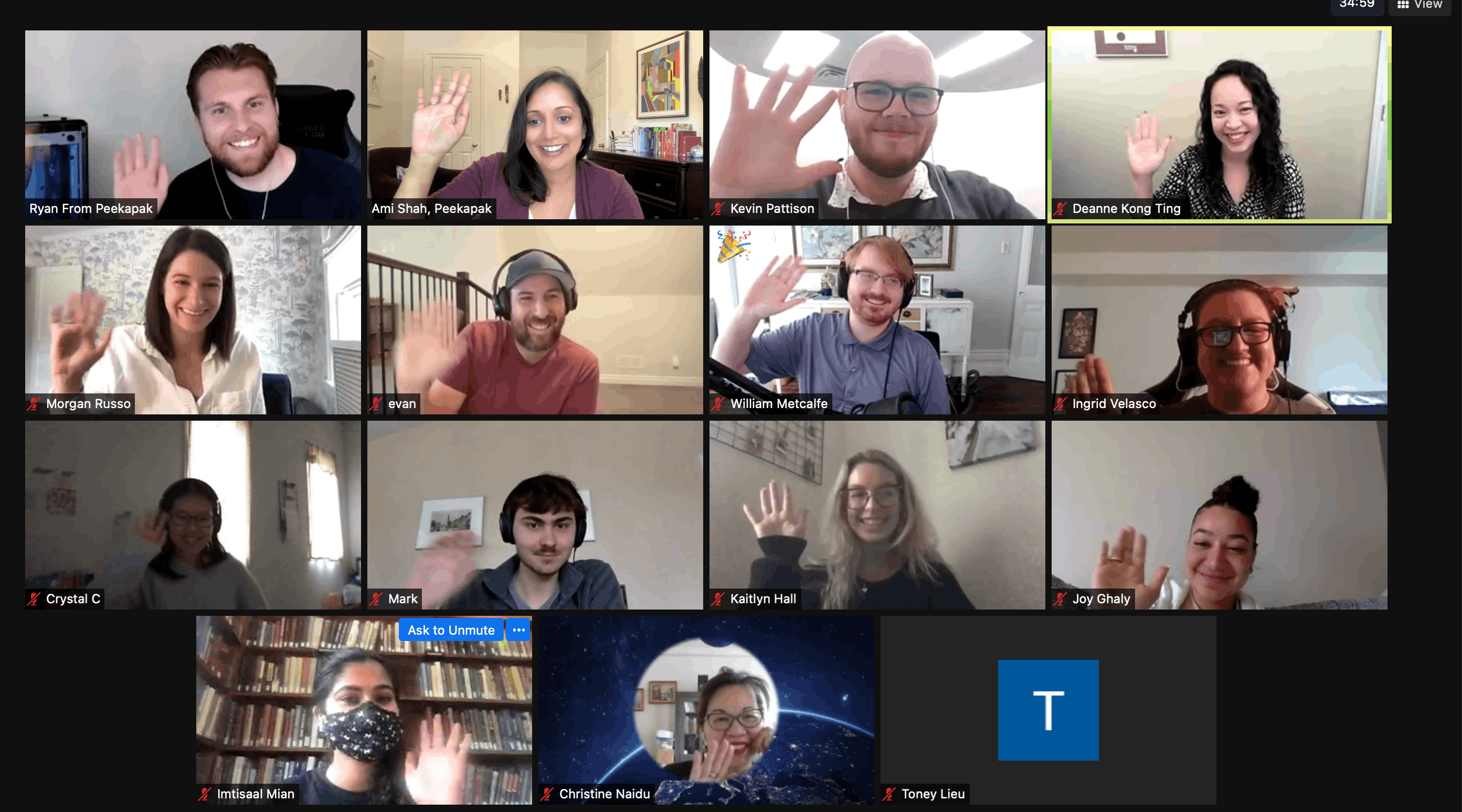 Screenshot of a Zoom video call with 16 participants, most of whom are smiling and waving at the camera in a friendly group gesture. The call interface shows a mix of home and office backgrounds, and some users have their microphones muted, as indicated by the red icons.