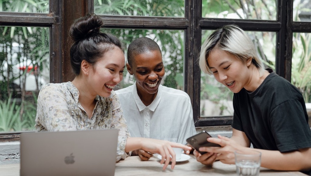 Diverse group of women enjoying smartphone browsing in a cozy cafe setting.