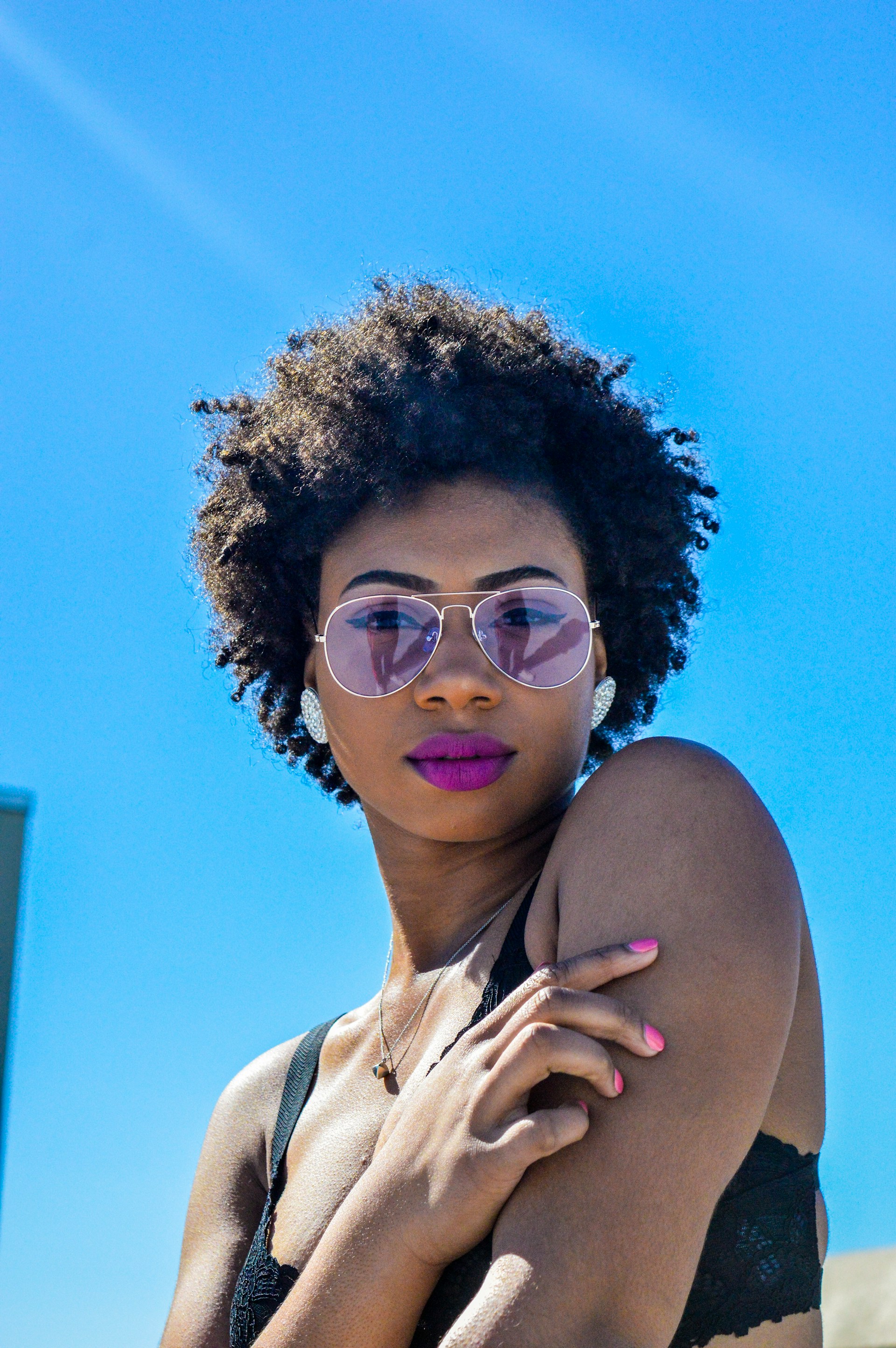 Woman with an afro and pink sunglasses against a blue sky.