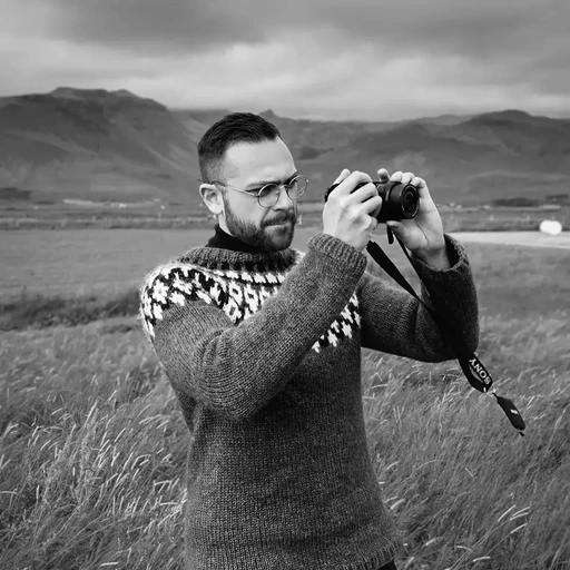 An image of Simon Kamali standing in a field in Iceland with mountains in the background.