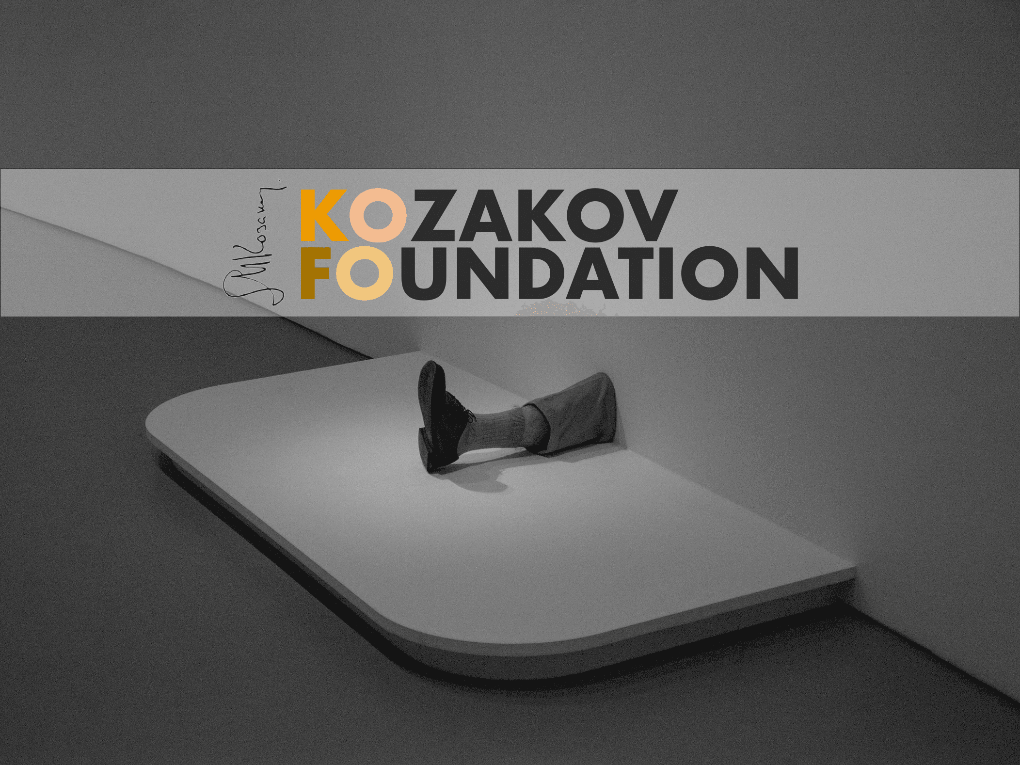 A colourful and black logo spelling "Kozakov Foundation" with a signature on the left side, designed by House Of Five Studio, on top of a black and white image of a leg sticking out of a wall wearing a sock and shoes, resting on a white surface.