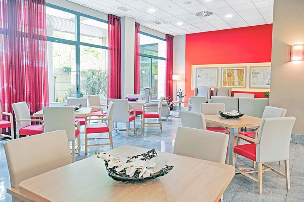 Bright modern interior living space with vibrant red accent walls, contemporary furniture including colorful seating, large windows with natural light, and open floor plan design