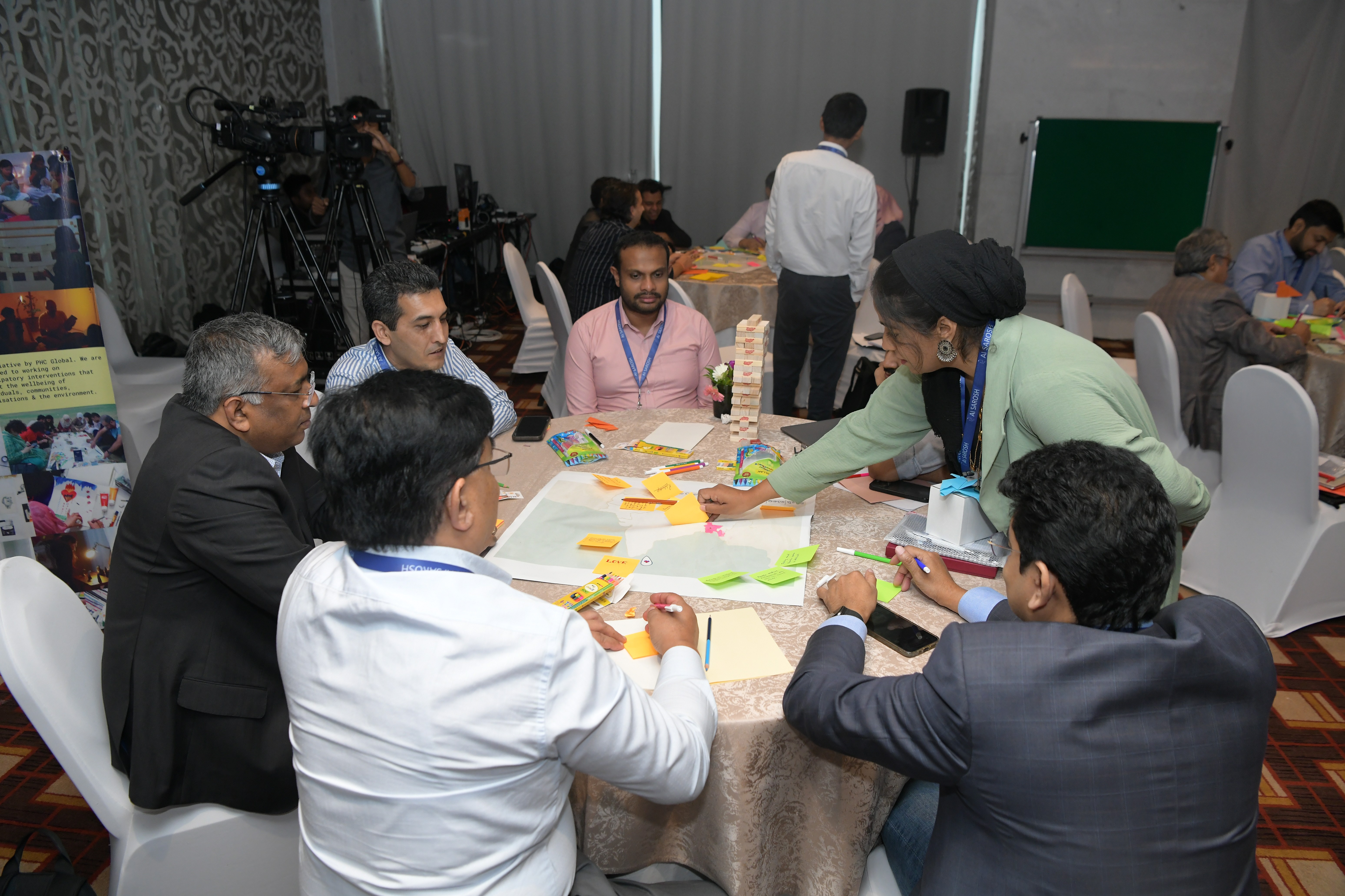 Participants sitting around a table ideating on artwork while Rutaba Syed of CFAW conducts a session