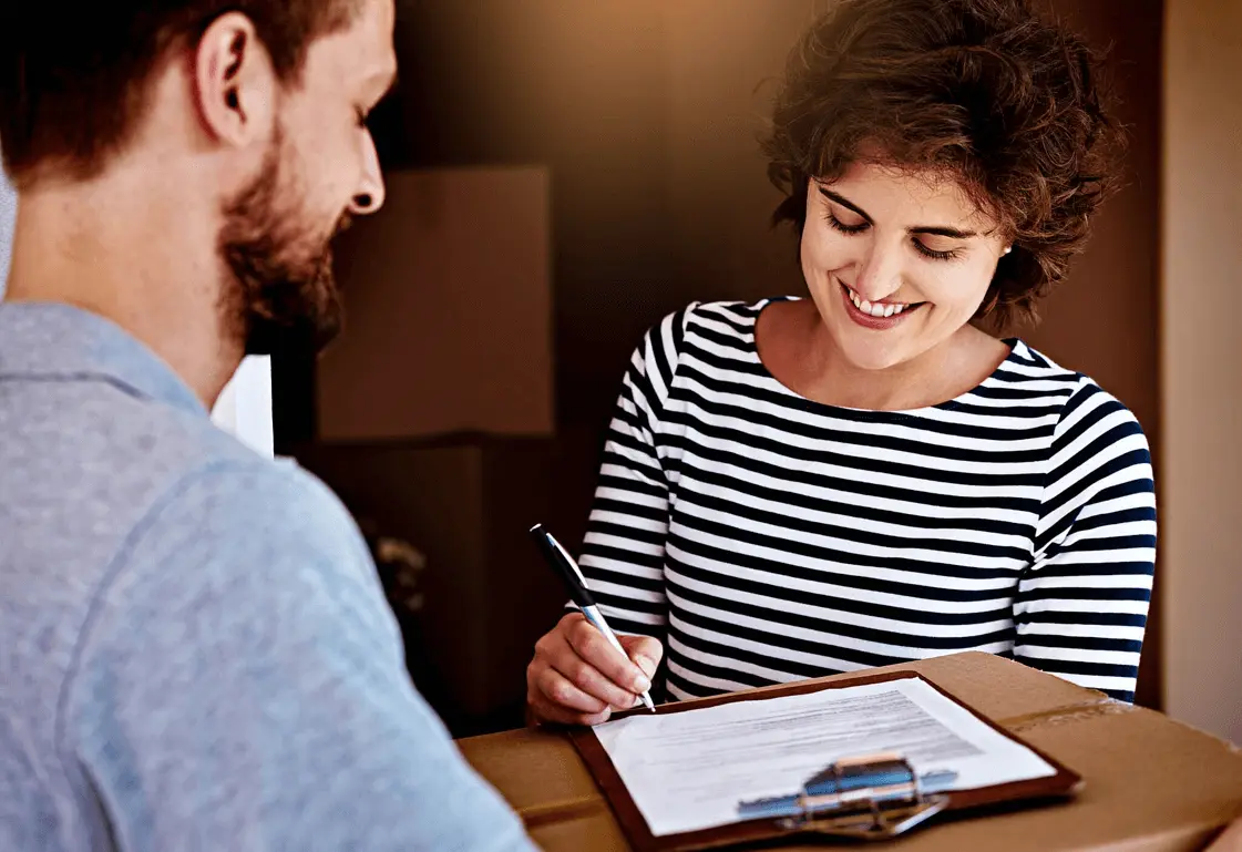 Smiling woman signing a delivery form on a clipboard held over a package handed by a courier