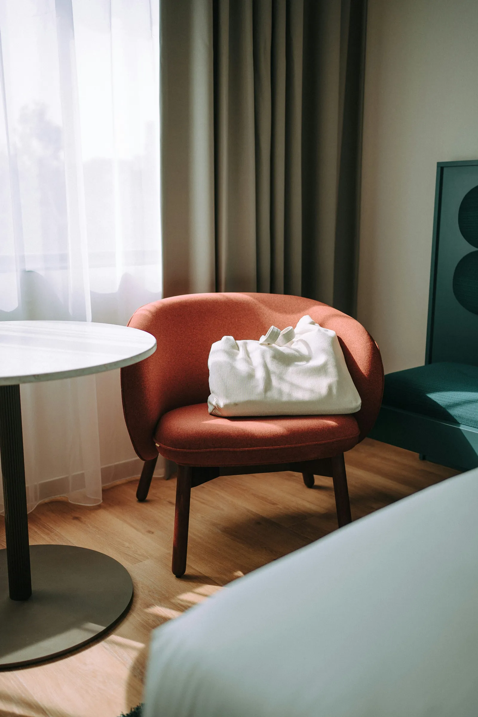 Hotel guestroom with a coral lounge chair, side table and oak floor