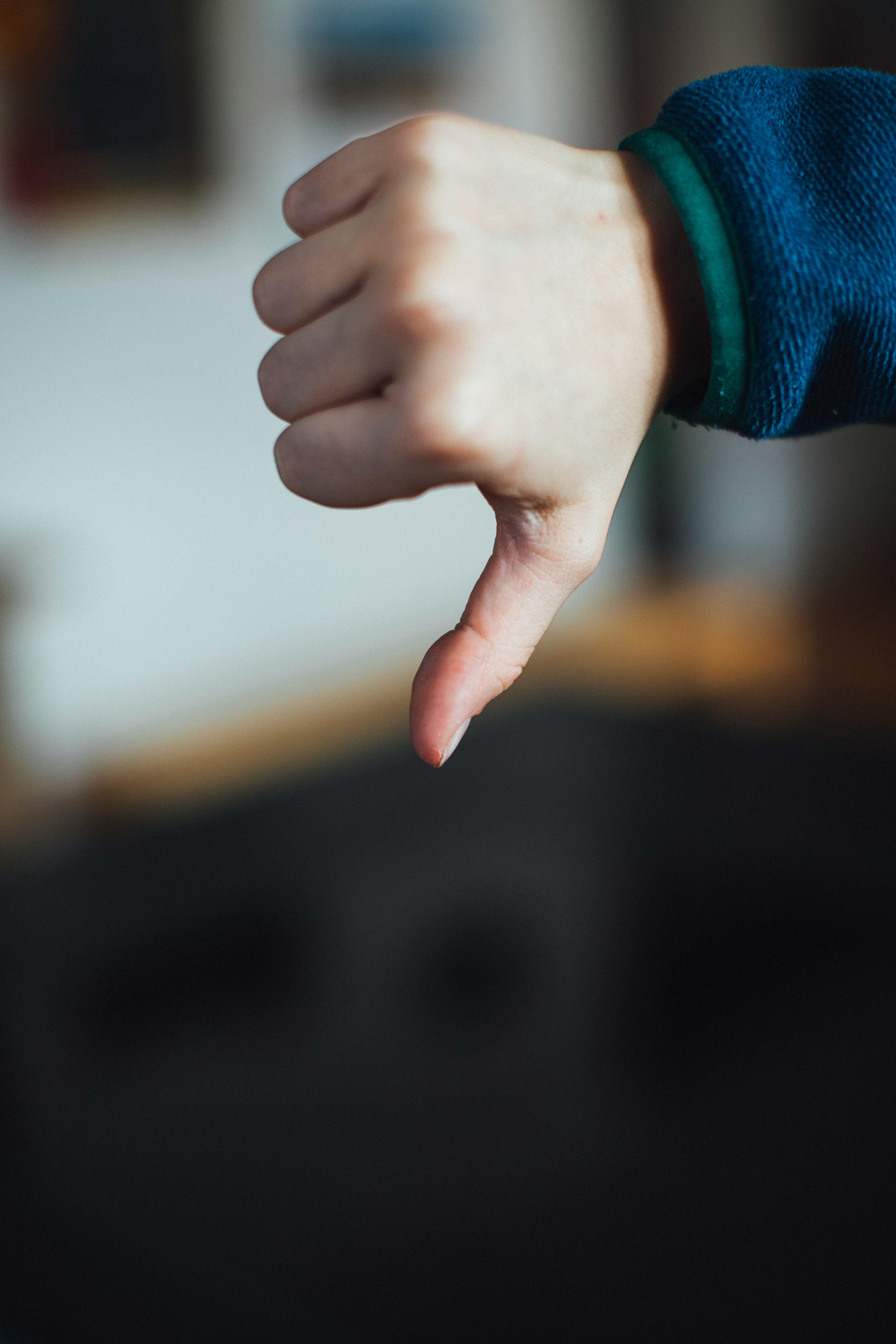 Close-up of a hand showing a thumbs down gesture, symbolizing disapproval or rejection.