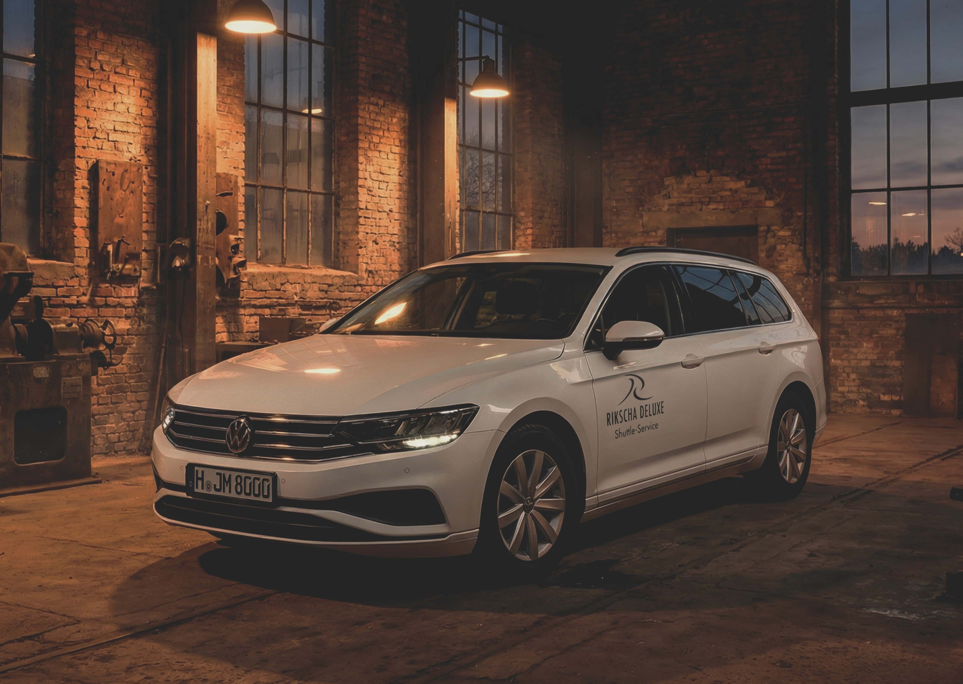 Ein weißer Volkswagen Kombi mit dem Logo „Rikscha Deluxe“ parkt in einer schwach beleuchteten Lagerhalle.