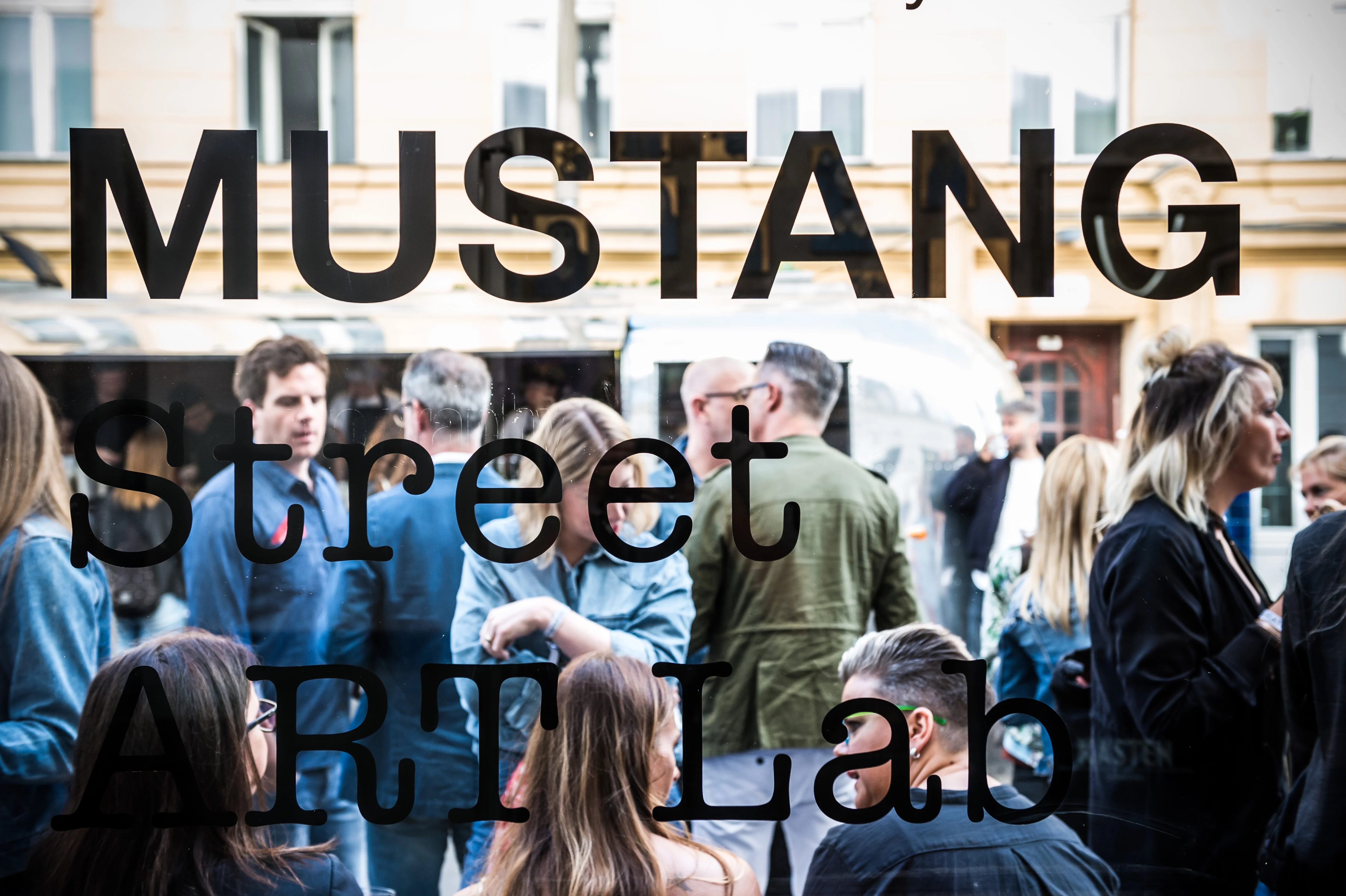 View through the window lettering MUSTANG Street ART Lab onto a crowd of guests at the event entrance.