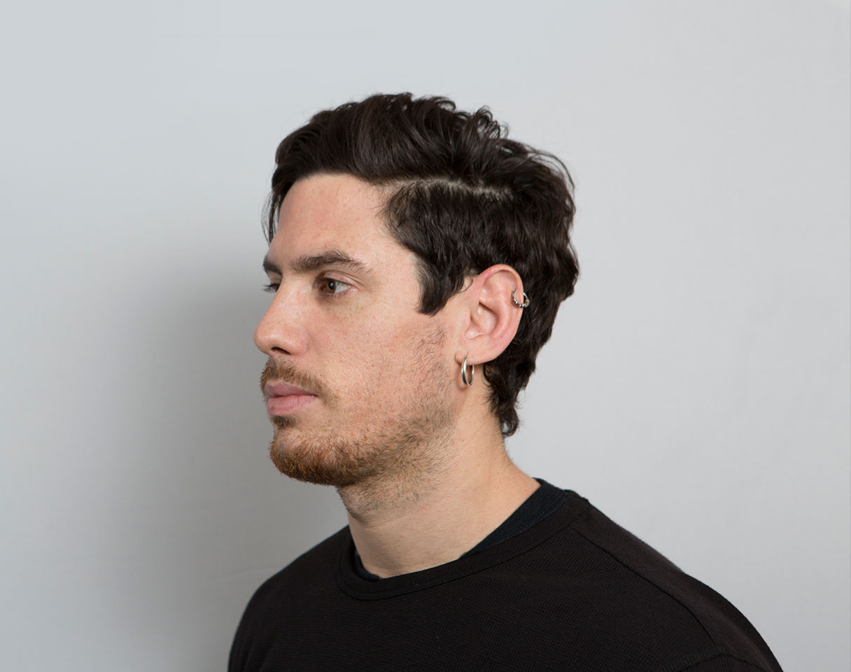 A thoughtful young person with dark hair gazes to the side, captured in soft black and white lighting.