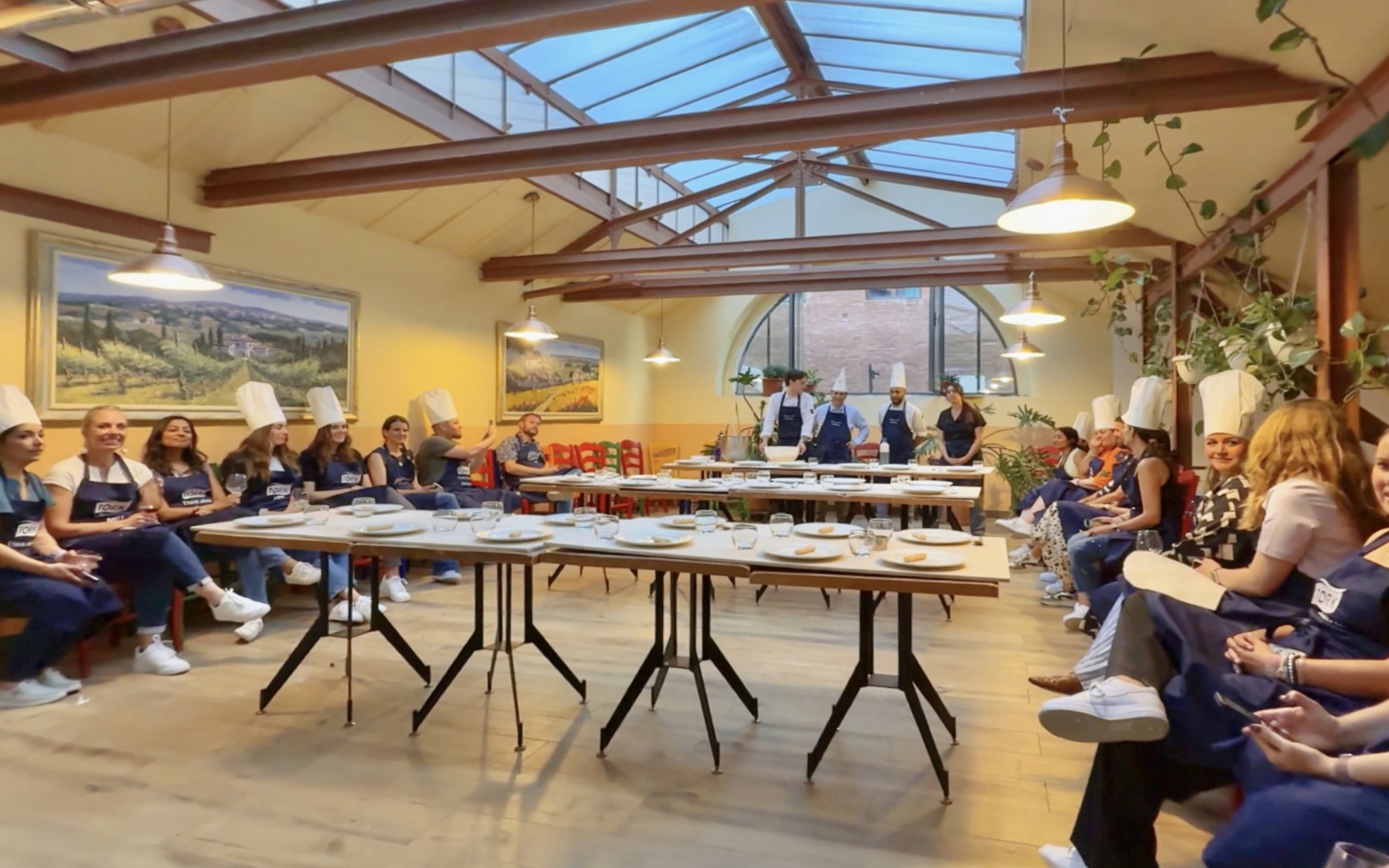 Participants in chef hats listening during a cooking class briefing in Siena.
