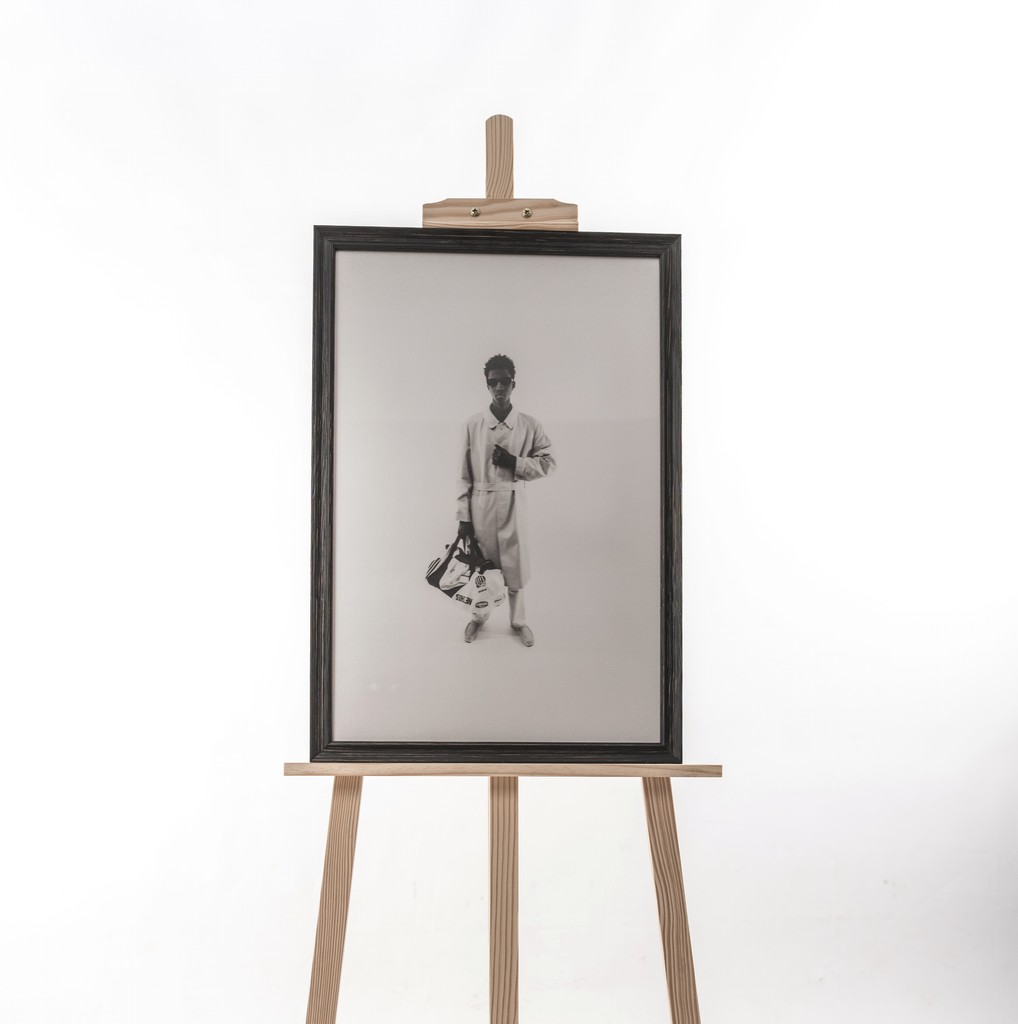 Framed black-and-white portrait presented on a wooden easel — minimalist composition radiating quiet power and refinement. Portrait encadré en noir et blanc présenté sur un chevalet en bois — composition minimaliste, empreinte de puissance silencieuse et de raffinement.