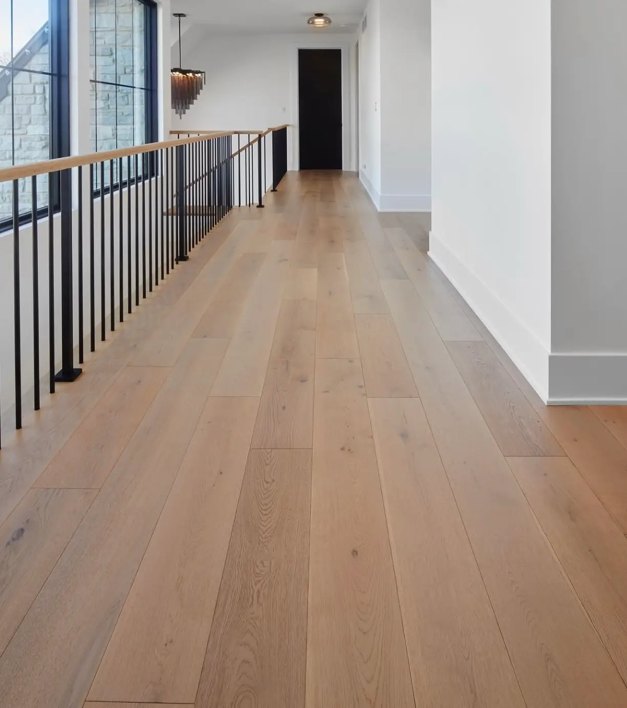 A long hallway showcasing dust-free light oak floors and polished white baseboards after a professional post-construction cleaning.
