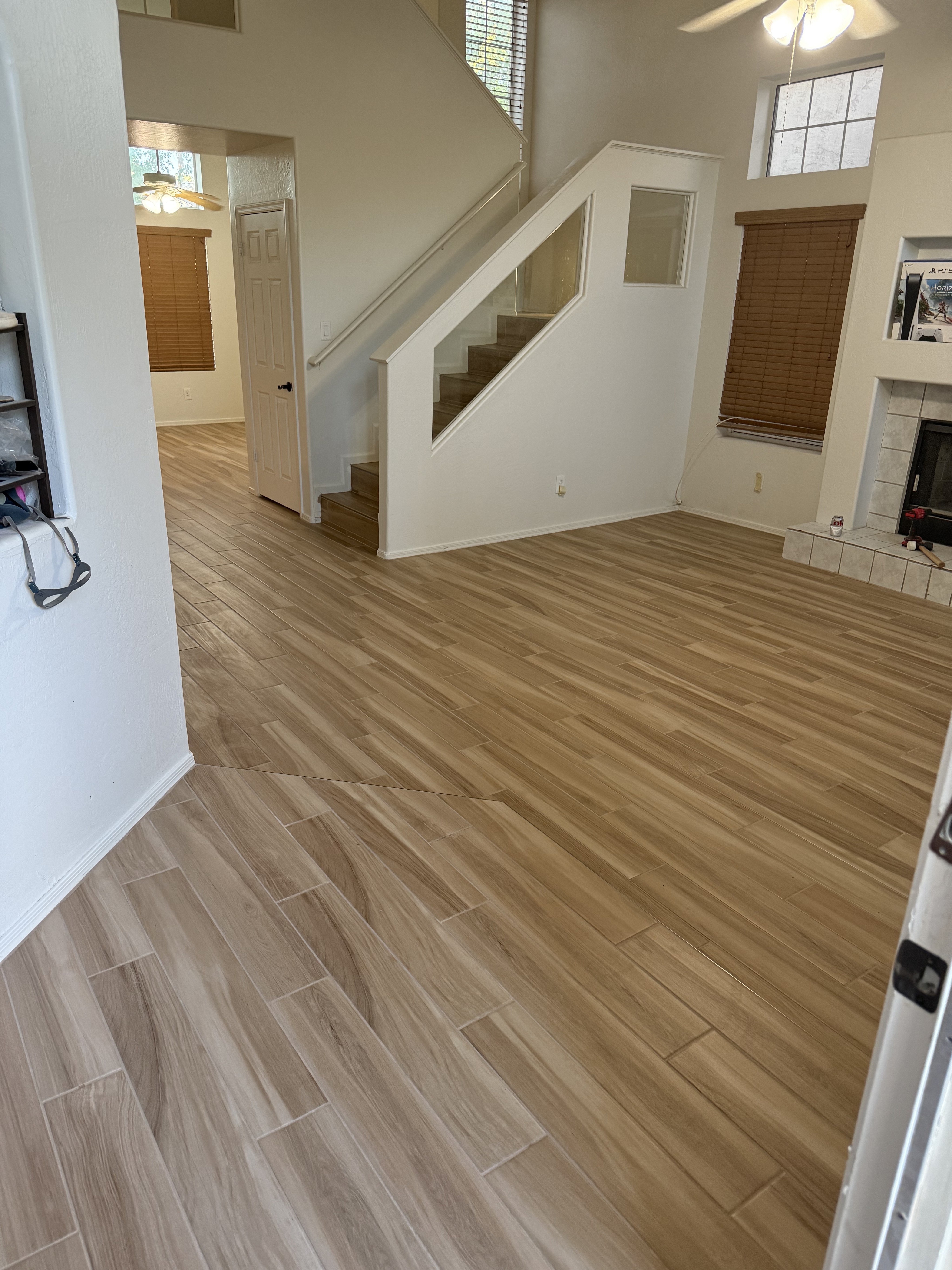 Modern living area with gray wood-look tile flooring, large sliding glass doors, and open space in a new home under construction.