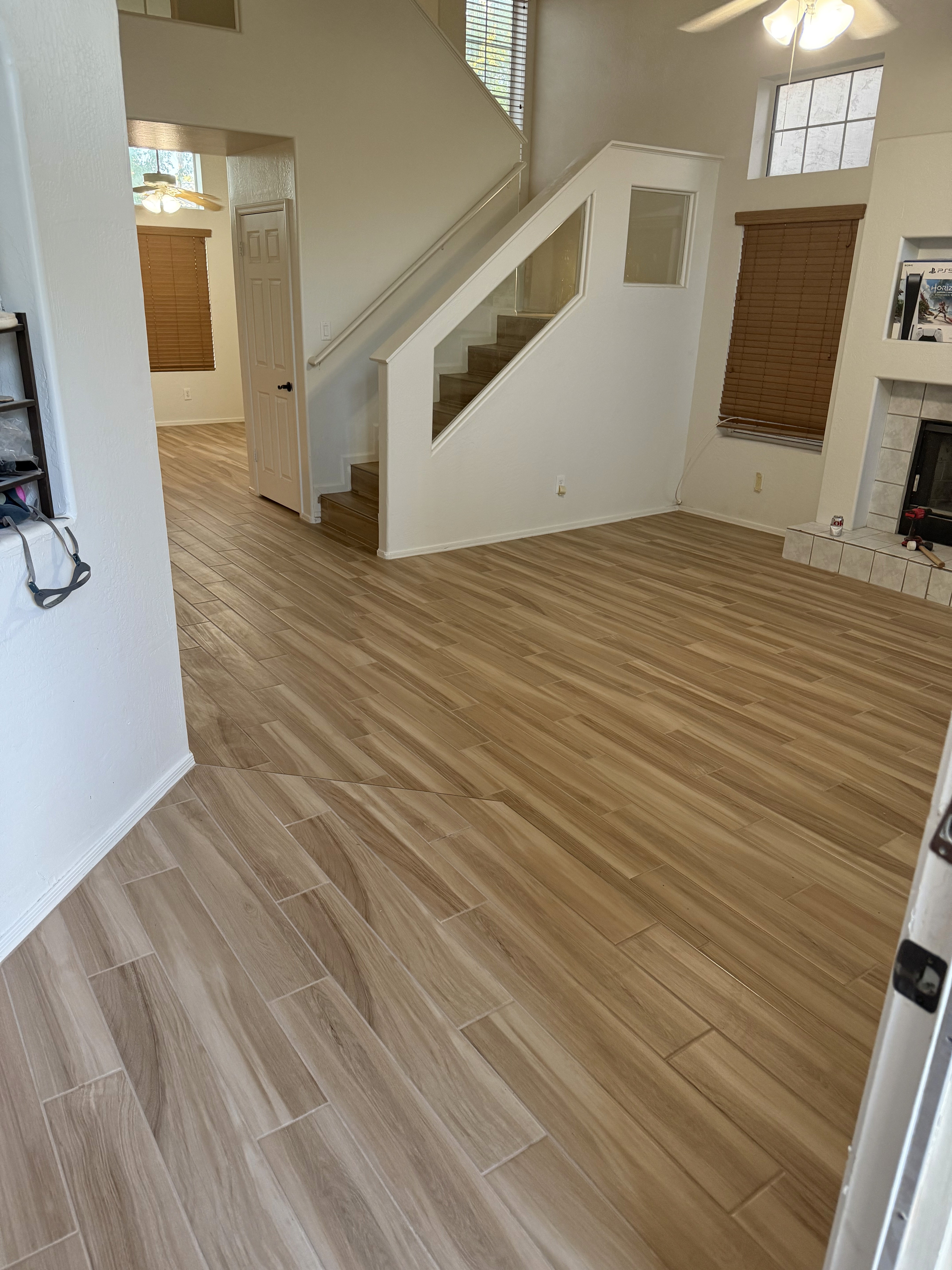 Modern living area with gray wood-look tile flooring, large sliding glass doors, and open space in a new home under construction.