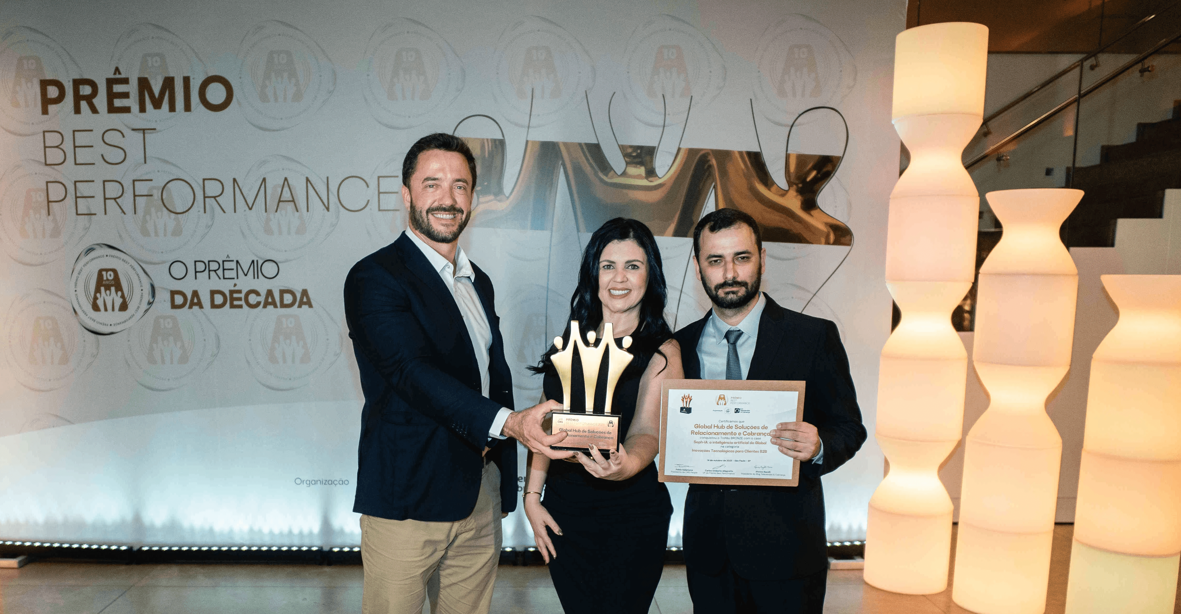 Executivos da Global Hub de Soluções de Relacionamento e Cobrança posando com troféu bronze e certificado no palco do Prêmio Best Performance 2025.