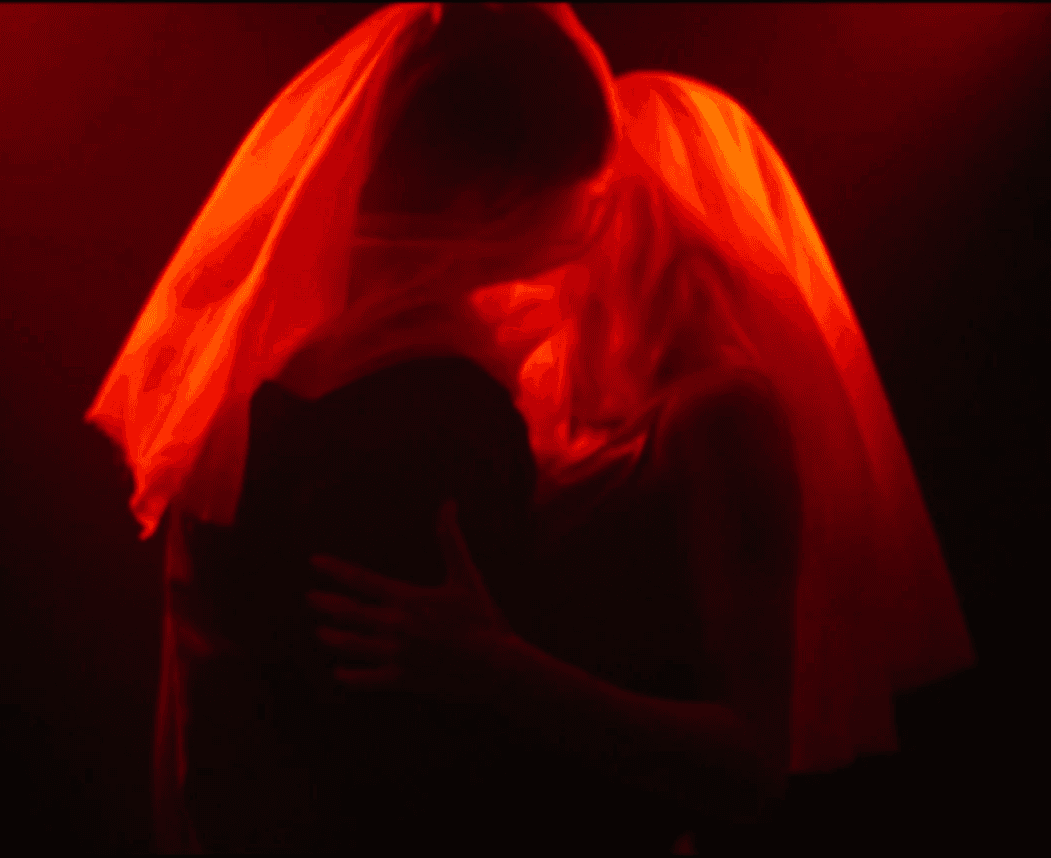 people under red curtain kissing