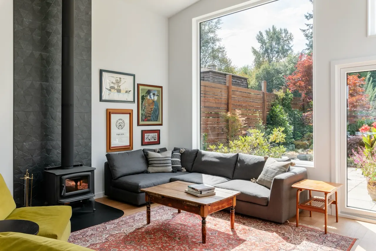 Modern two-story home with large glass windows, warmly lit interiors, and a balcony. Surrounded by trees and a manicured lawn at dusk. Cozy ambiance.