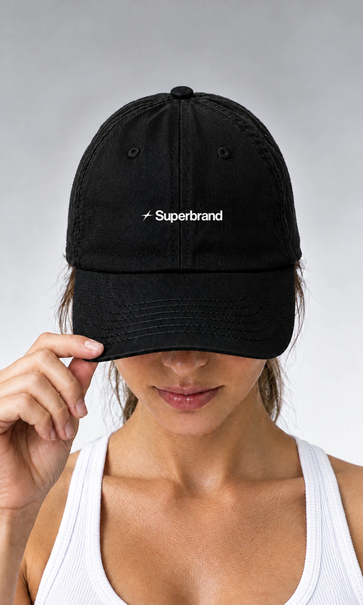 A woman in a white vest pulling a black Superbrand cap down over her eyes.