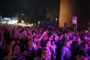 Dichtes Publikum bei Nacht, warmes Licht von der Bühne.