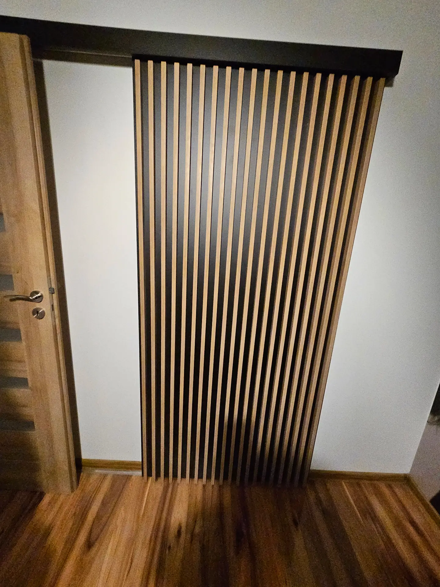 Drzwi przesuwne z drewnianych lameli w nowoczesnym korytarzu z drewnianą podłogą.