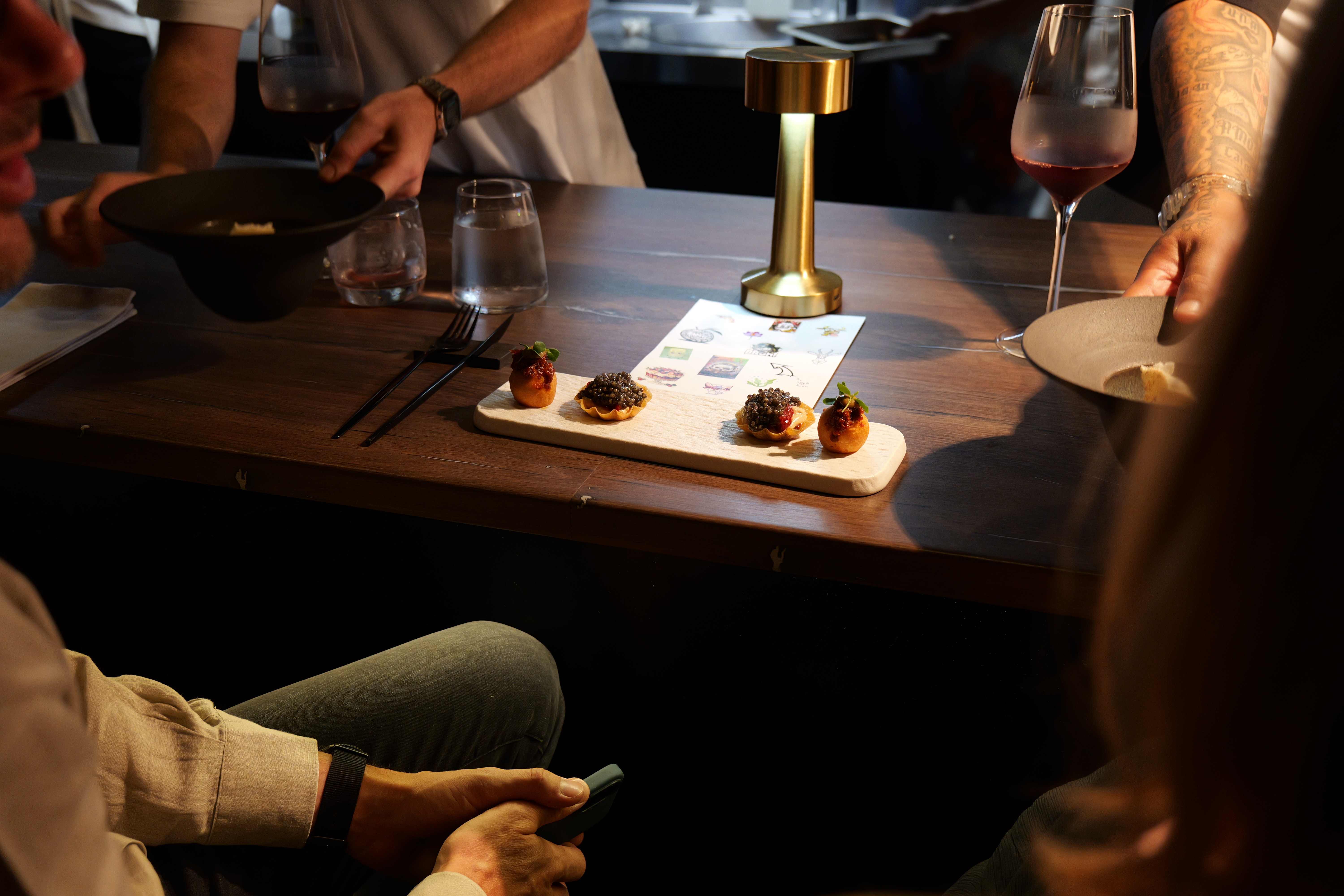 White plate with roasted chicken served in a golden sauce with herbs and capers, placed on a terrazzo tabletop in sunlight.