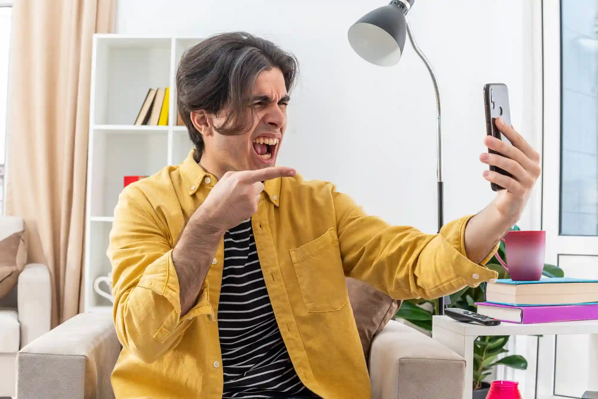 Frustrated man pointing angrily at his smartphone during a video call or viewing an error message.