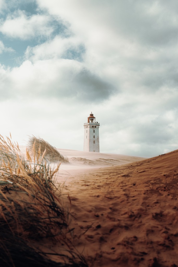 A beach on a partly cloudy day with a lighthouse standing in the distance