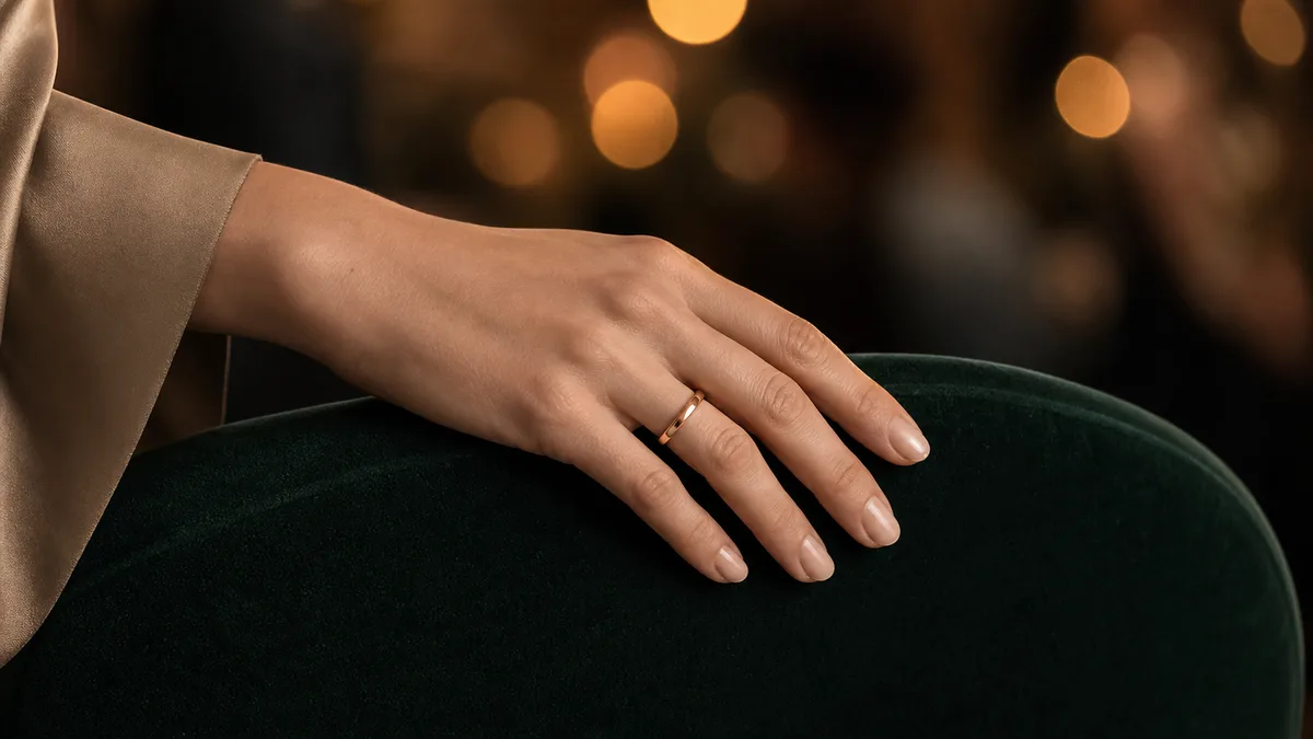 Hand wearing a plain rose-gold smart dhikr ring on a dark green velvet chair