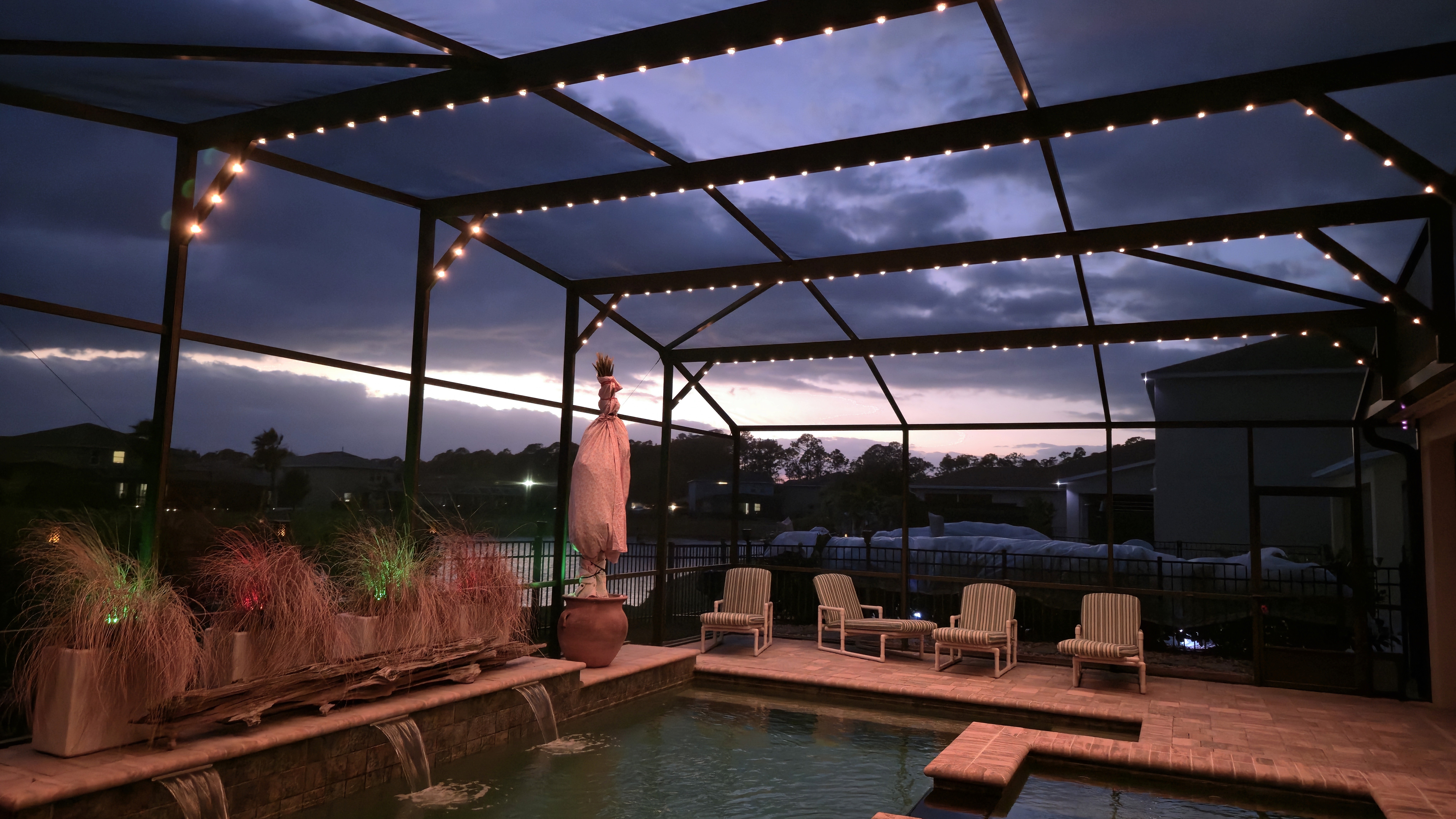 Warm patio lighting installed inside screened lanai pool enclosure at sunset