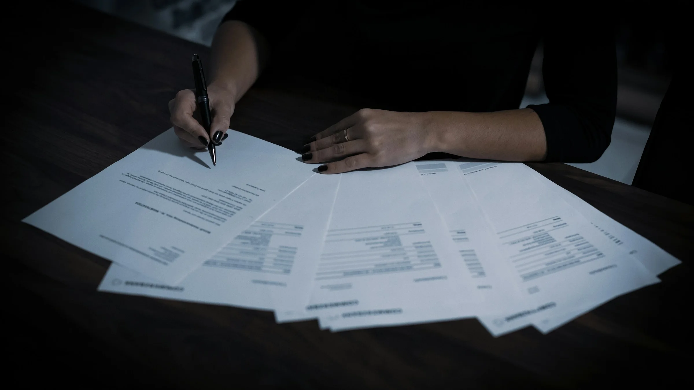 A person signing a stack of tax forms spread across a dark table